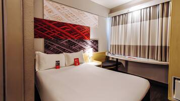 A hotel room with a bed, a desk, and a window with curtains.