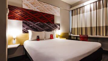 A hotel room with a large bed, two bedside tables with lamps, a window with curtains, and a wall with a patterned design.