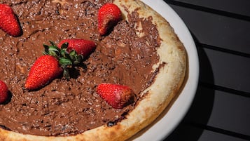 Eine mit Schokolade überzogene Pizza auf einem weißen Teller, dazu Erdbeeren auf dunklem Untergrund.