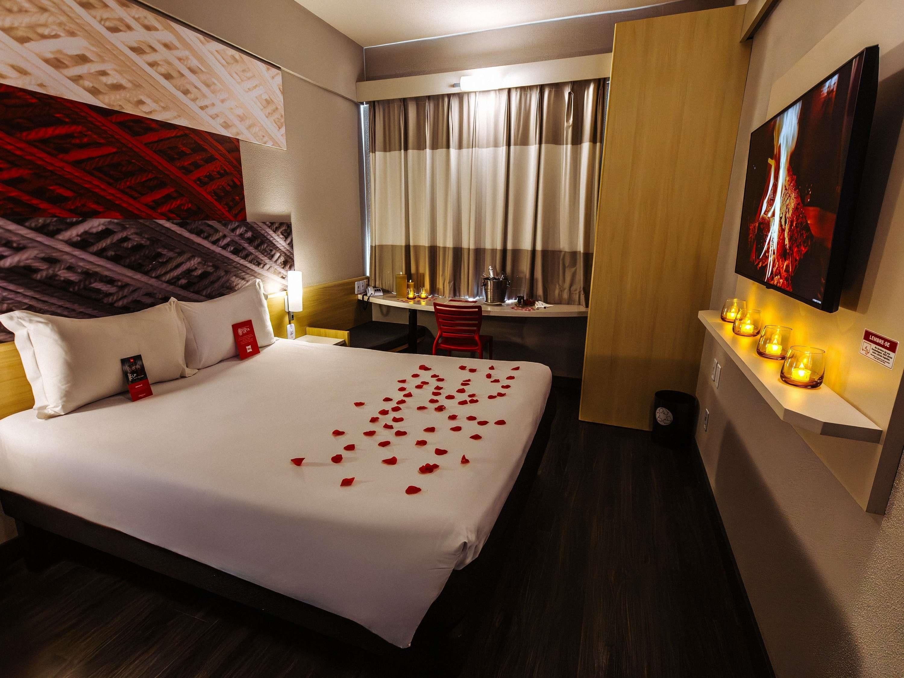 Habitación de hotel con cama, escritorio, silla, televisión y estante en la pared con velas.