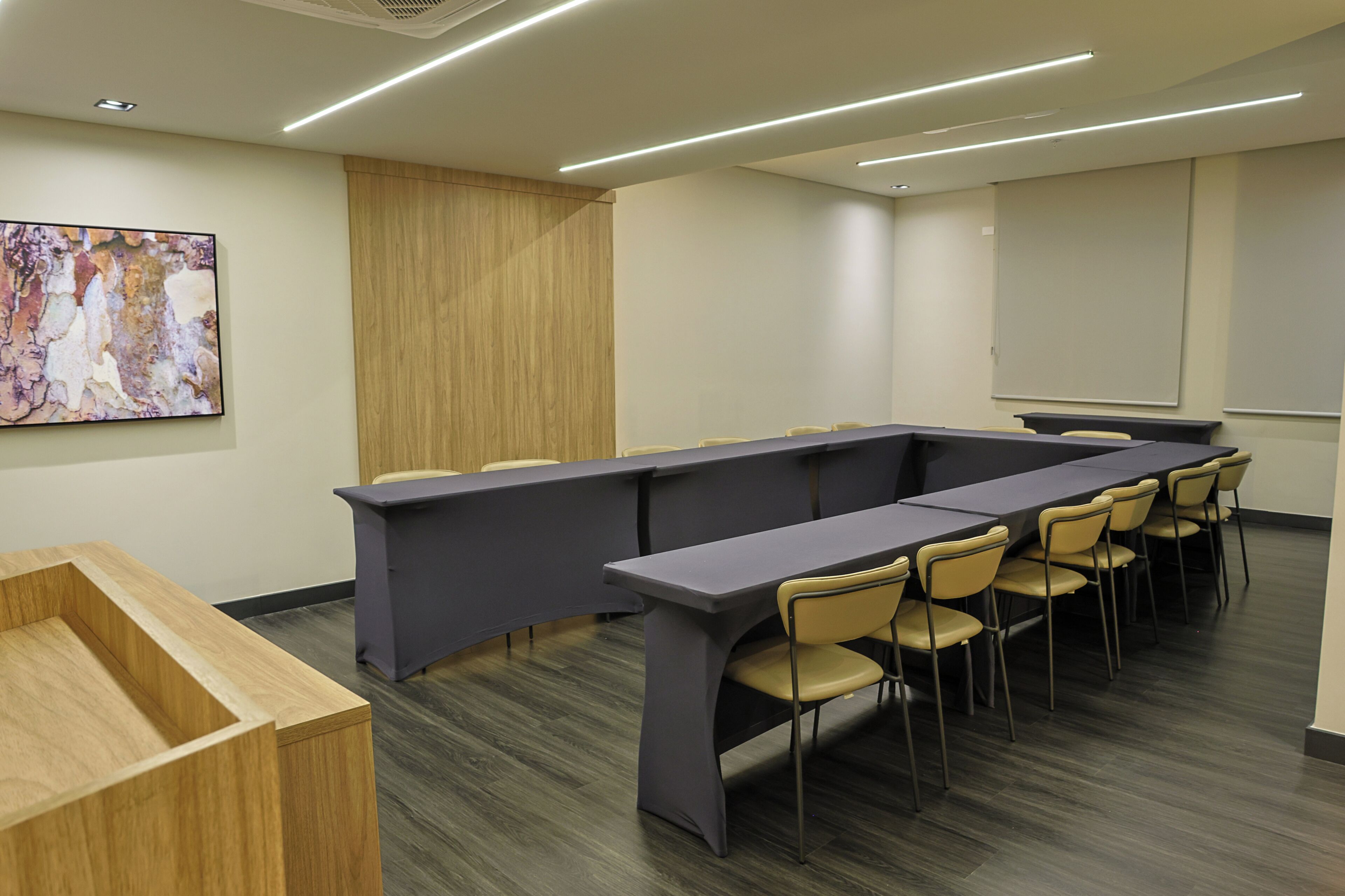 Un salón de conferencias con una larga mesa, sillas, una pantalla de proyector y un armario de madera.