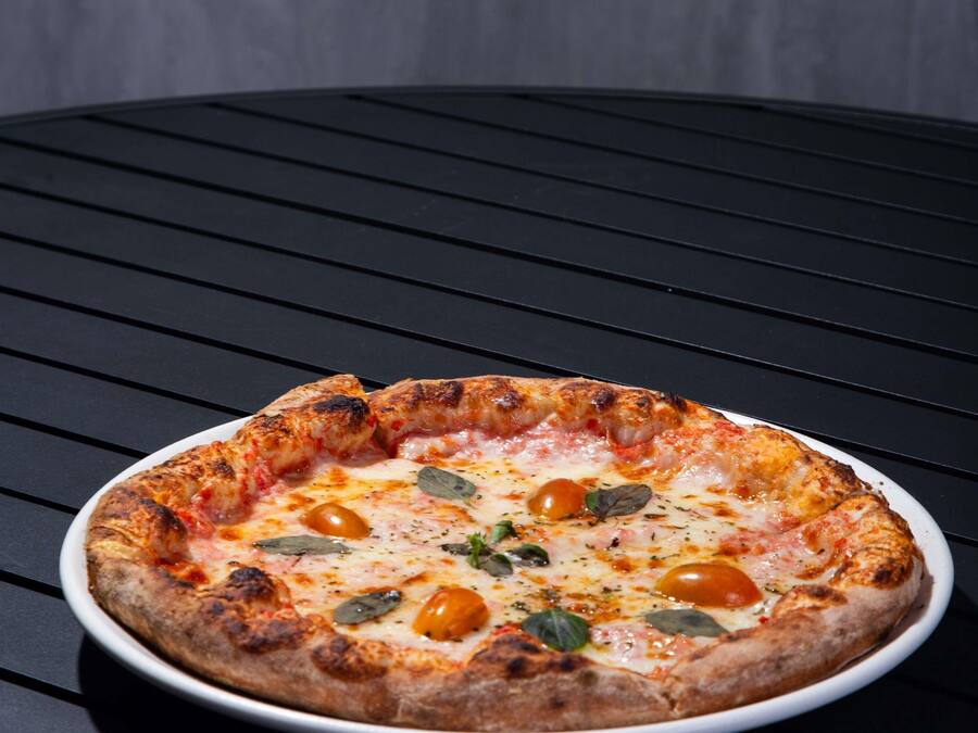 Eine Pizza auf einem weißen Teller auf einem schwarzen Tisch.