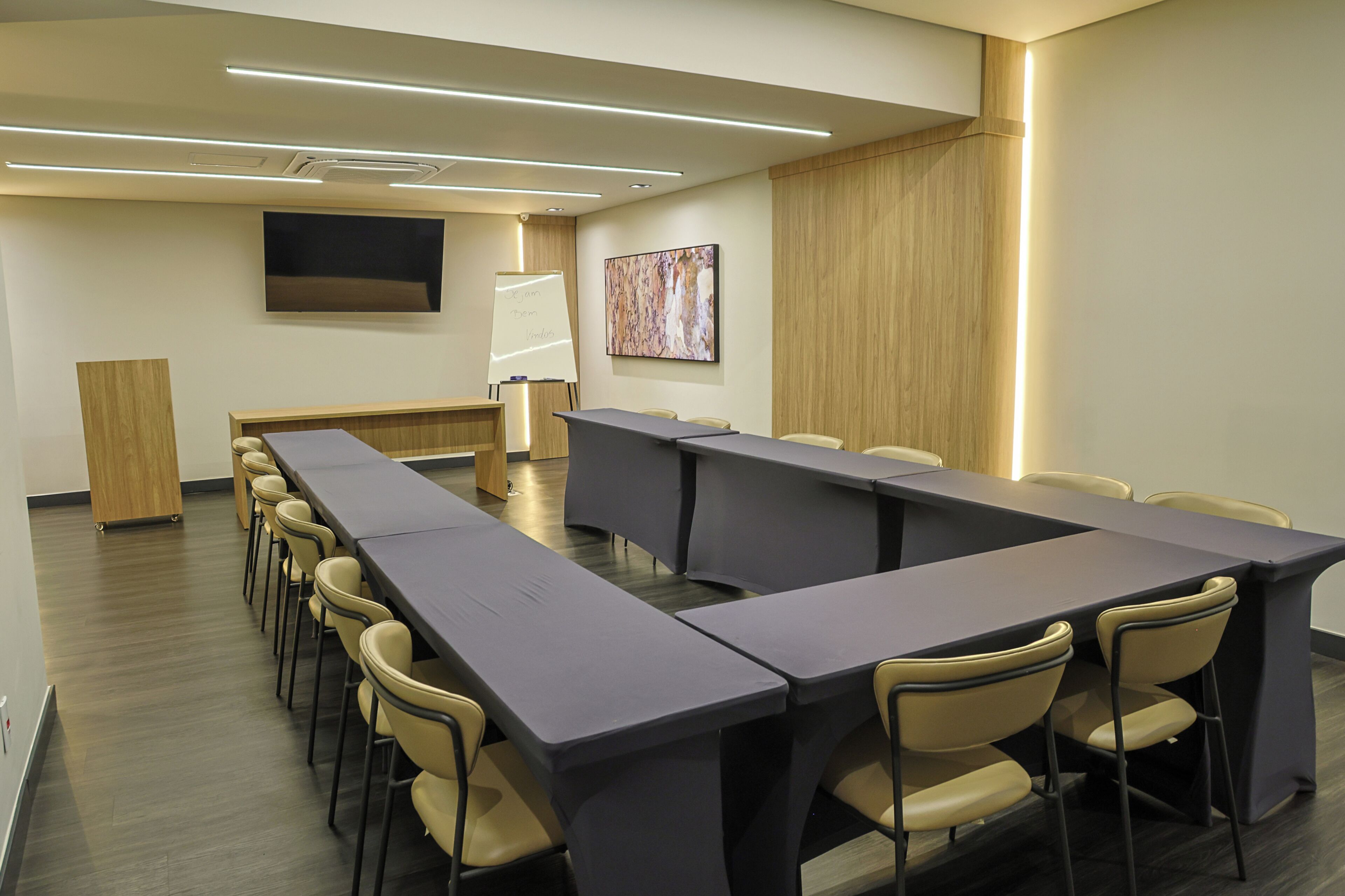 A conference room with a long table, chairs, a whiteboard, and a flat-screen TV on the wall.