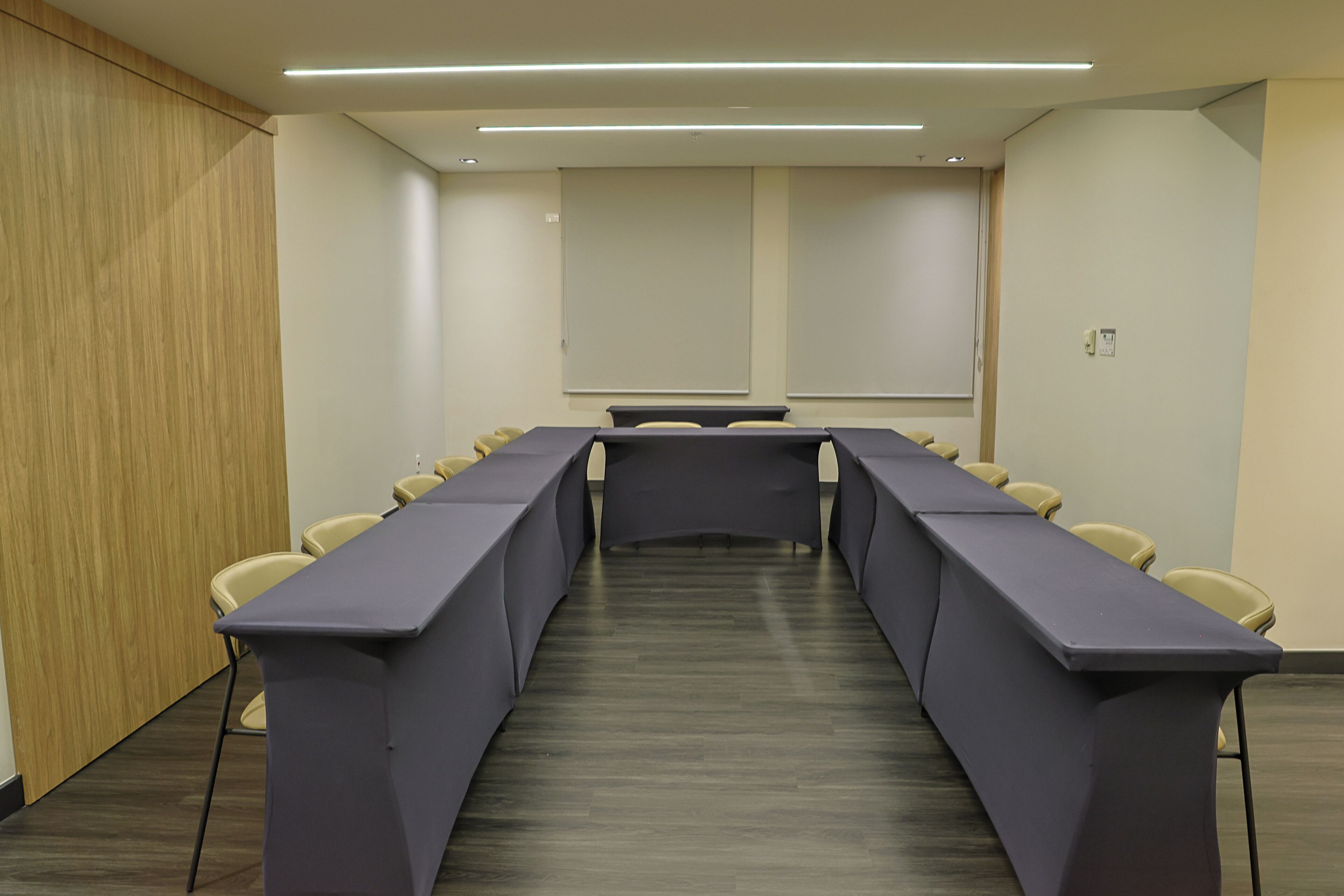 A conference room with a long table, chairs, a projector screen, and a wooden panel wall.