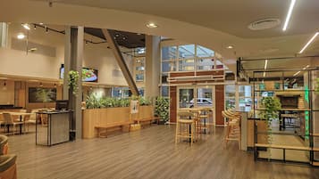 Un interior moderno con suelo de madera, zonas de estar y una cocina con cafetera.