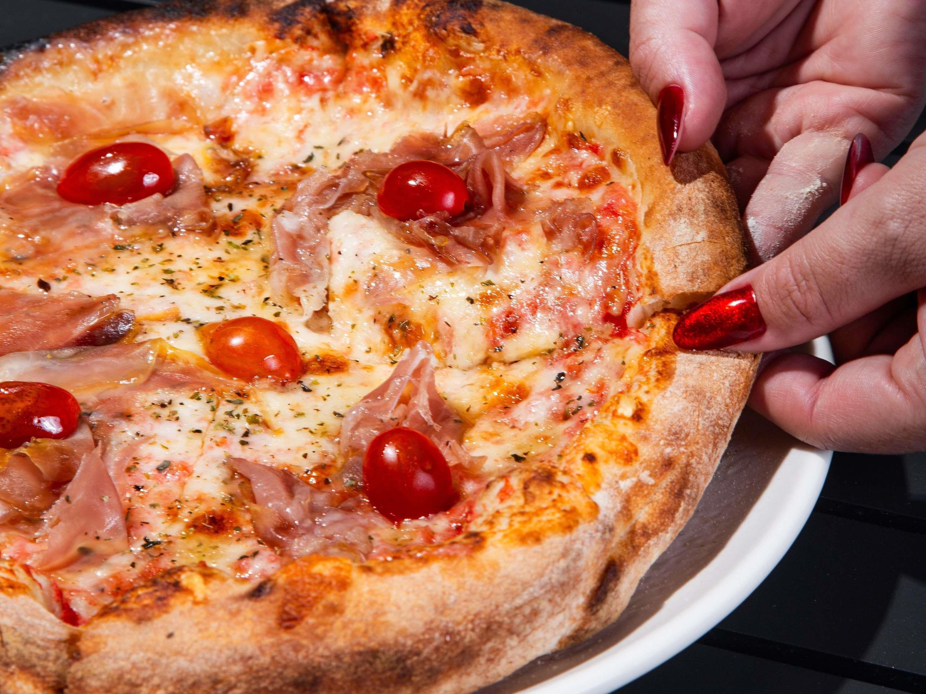 Eine Pizza mit Belag, die von einer Hand gehalten wird.