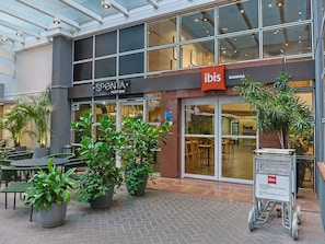 A modern building with a glass facade, a pizza bar named 'SPONTA,' and a sign for 'ibis.'