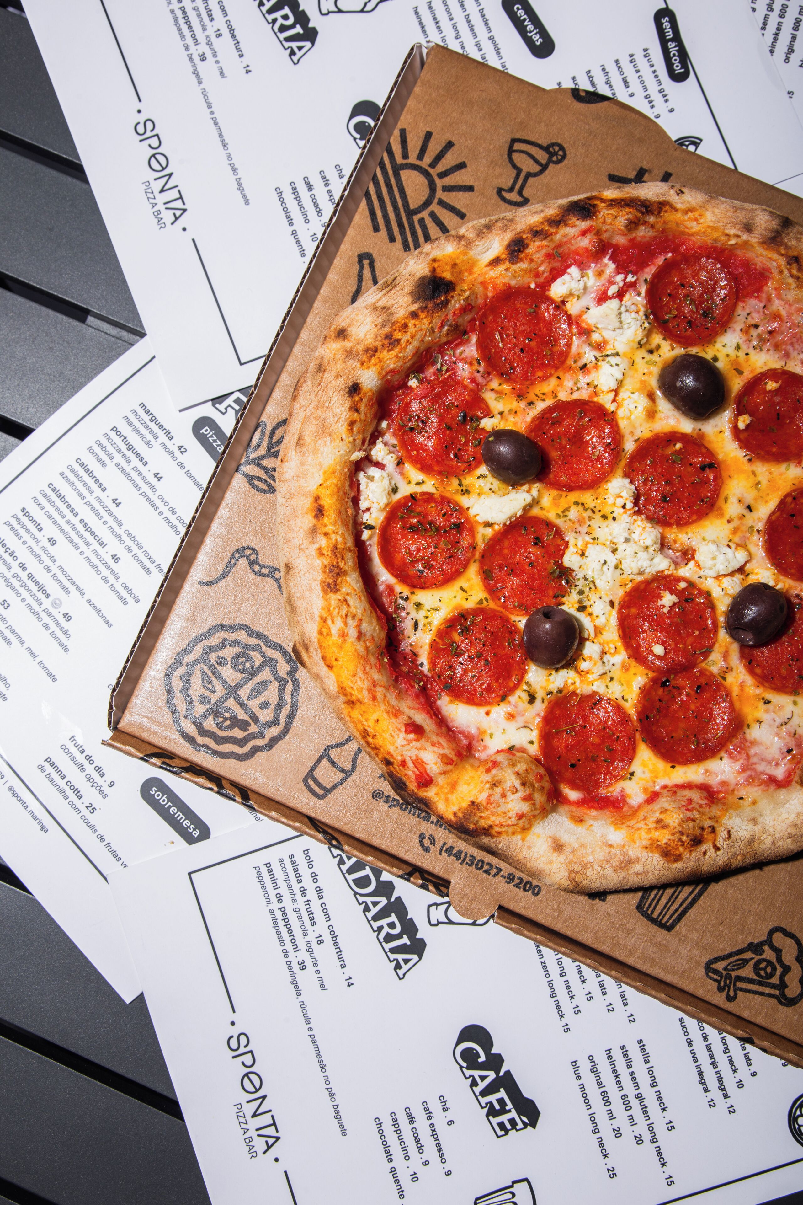 Una caja de pizza con una pizza de pepperoni encima, sobre una mesa con menús impresos.