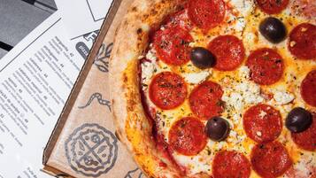 Una caja de pizza con una pizza de pepperoni encima, sobre una mesa con menús impresos.