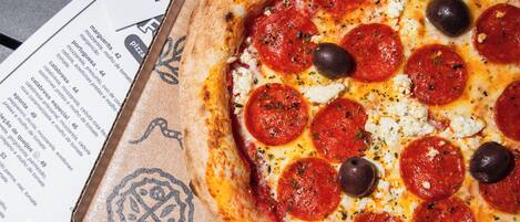 Una caja de pizza con una pizza de pepperoni encima, sobre una mesa con menús impresos.