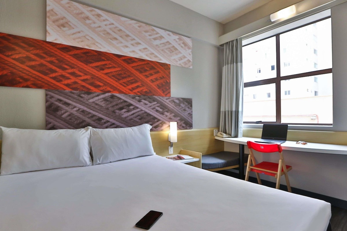 A hotel room with a bed, a desk, a chair, and a window.