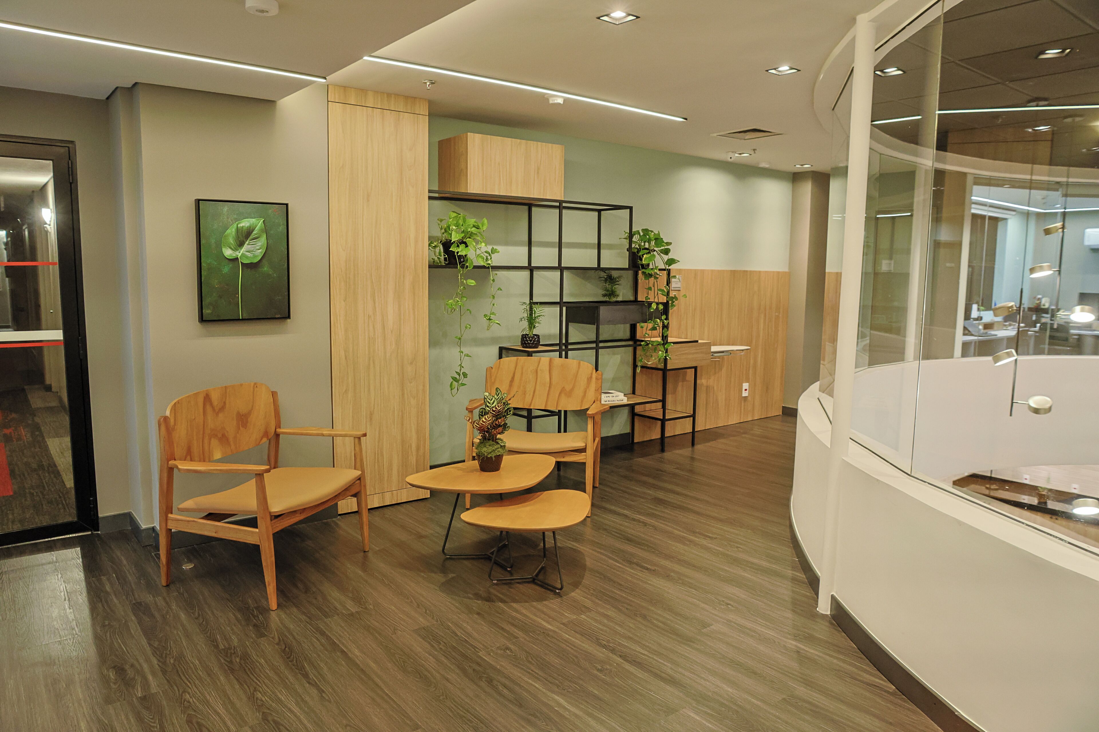 A modern office space with wooden furniture, a glass partition, and potted plants.