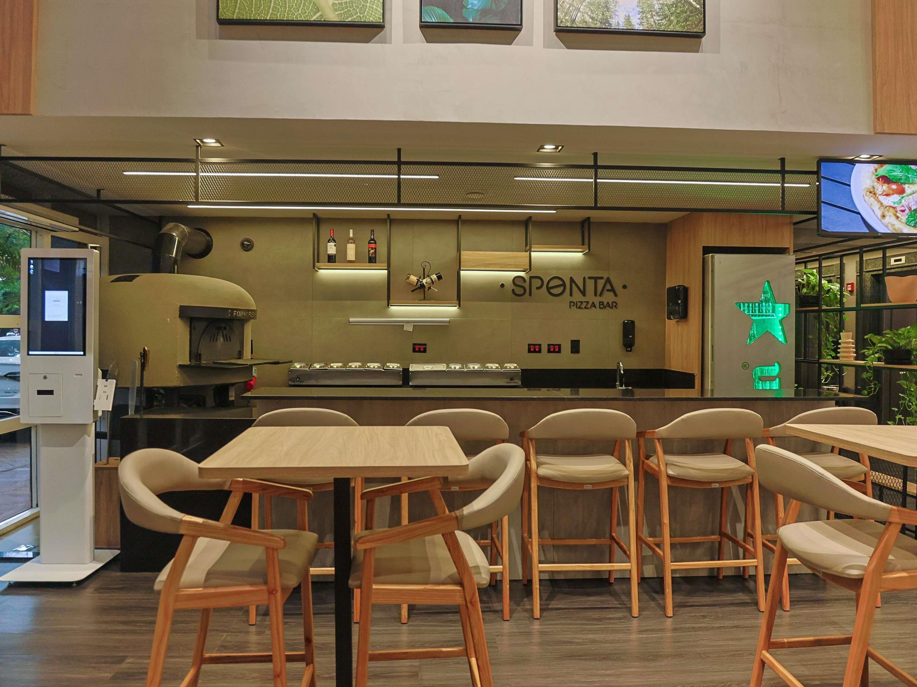 A pizza bar with a counter, chairs, and a neon sign.