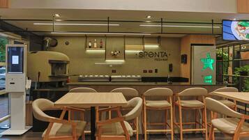 A pizza bar with a counter, chairs, and a neon sign.