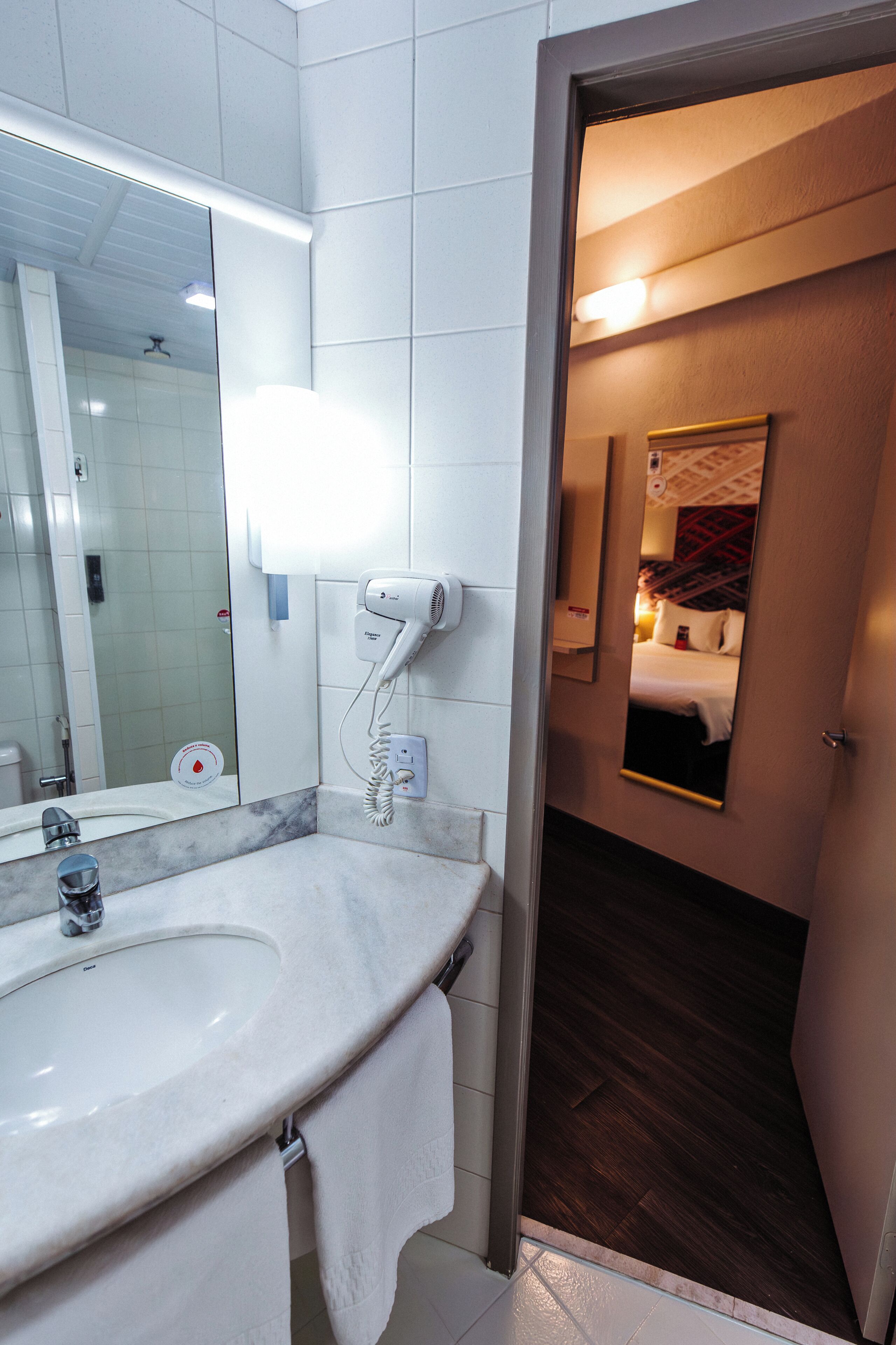 A hotel bathroom with a sink, mirror, and hairdryer.