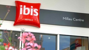 Une enseigne d’hôtel indiquant « ibis Hotels » et une autre indiquant « Millau Centre », au-dessus de l’entrée d’un immeuble.