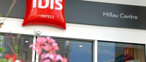 A hotel sign for 'ibis Hotels' and a 'Millau Centre' sign above a building entrance.