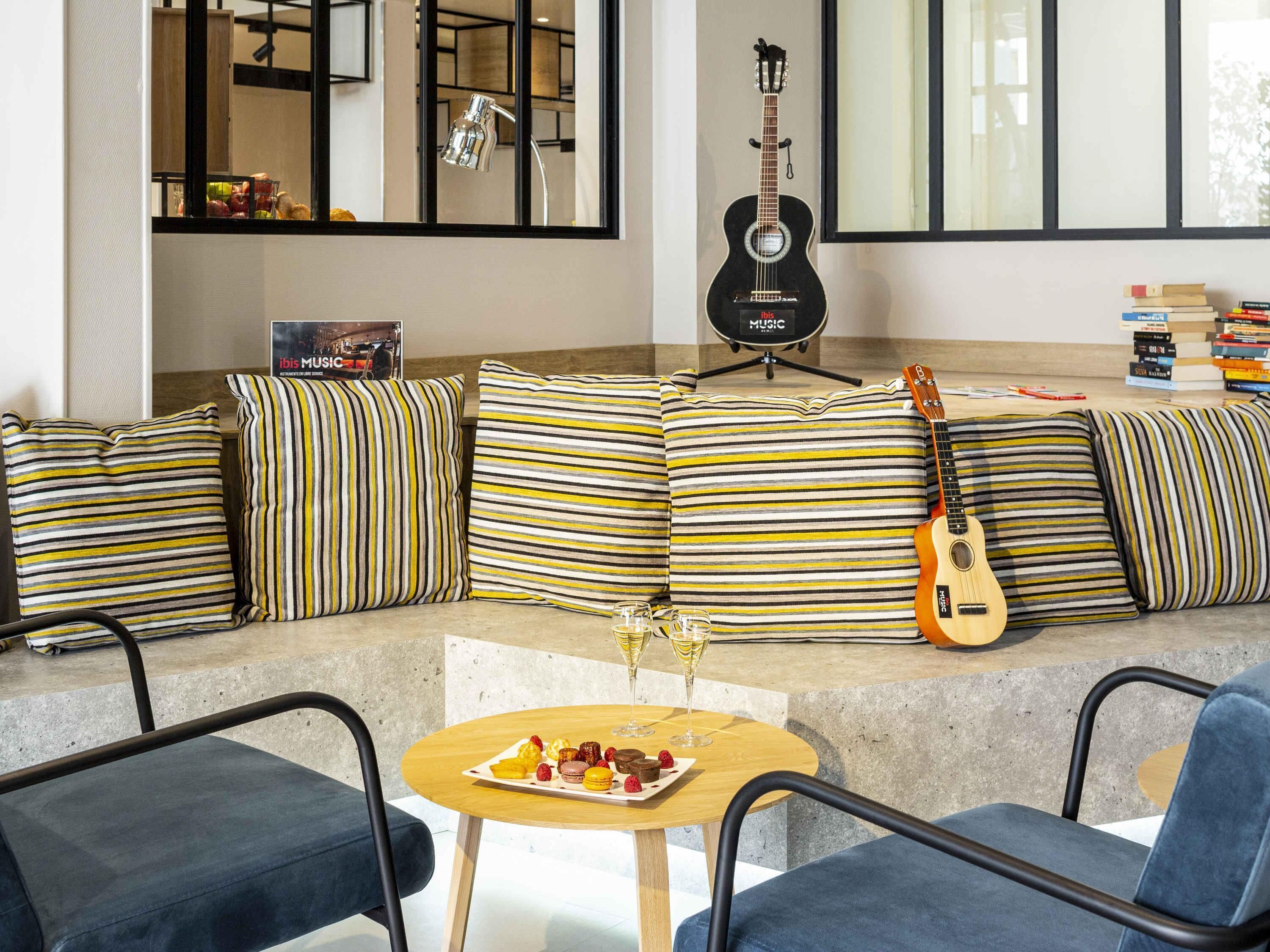 A modern living area with a sofa set, a guitar, a small table with snacks, and a bookshelf.