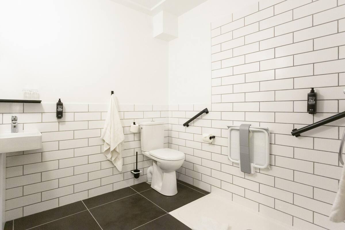 Un baño moderno con azulejos blancos tipo metro, un inodoro blanco, un lavamanos y una toalla colgada en la pared.