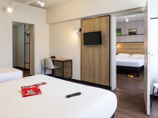 A hotel room with a bed, a desk with a chair, a TV mounted on the wall, and a wardrobe. - ibis Millau (Millau)