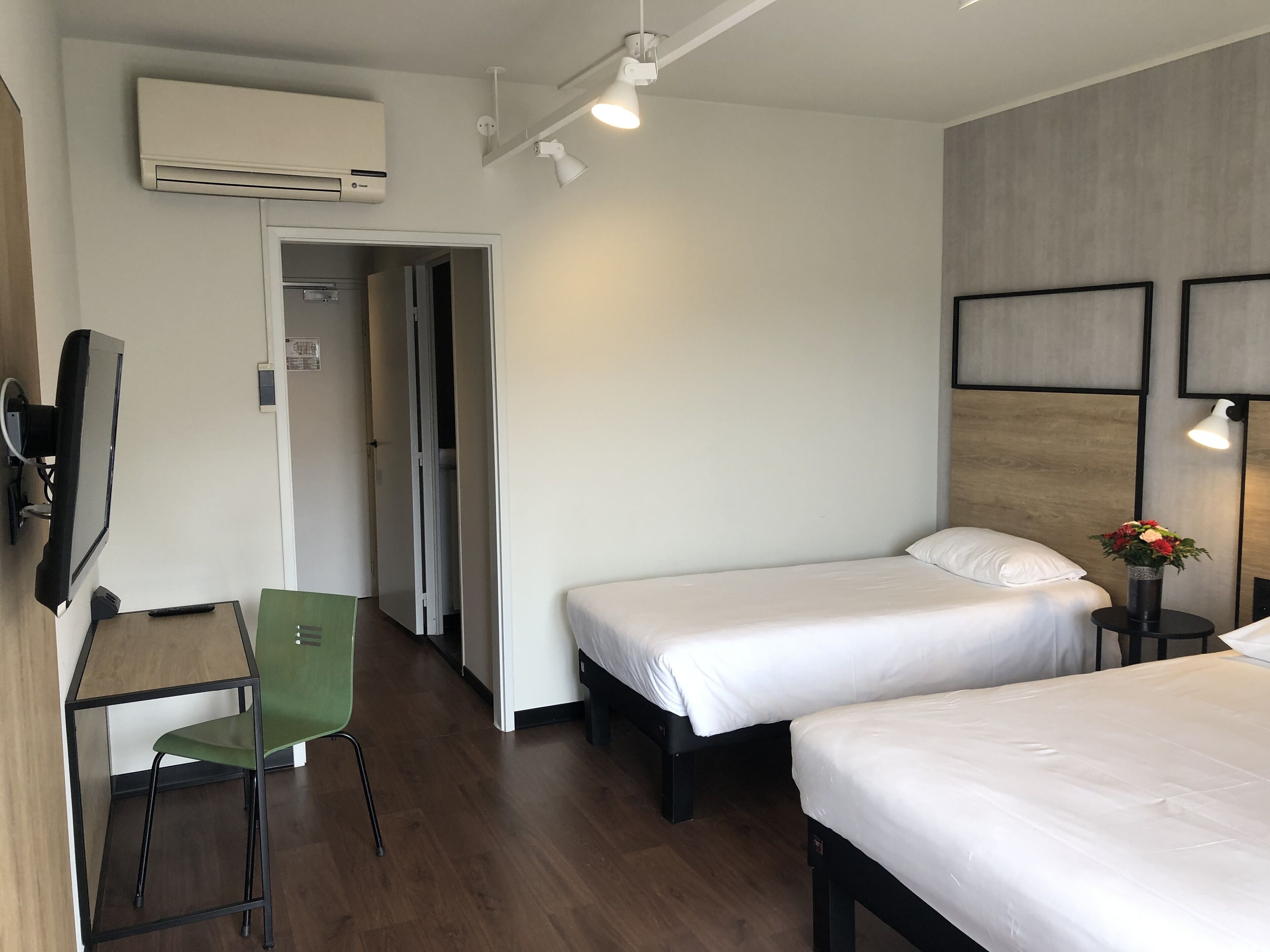 Et hotelværelse med to senge, et skrivebord med stol, en aircondition og et fjernsyn.