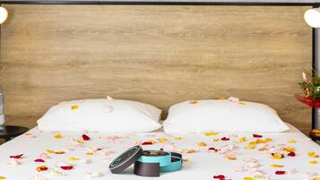 Ein Bett mit Rosenblättern auf der Bettdecke, zwei Kissen und ein kleiner blauer Behälter auf dem Bett.
