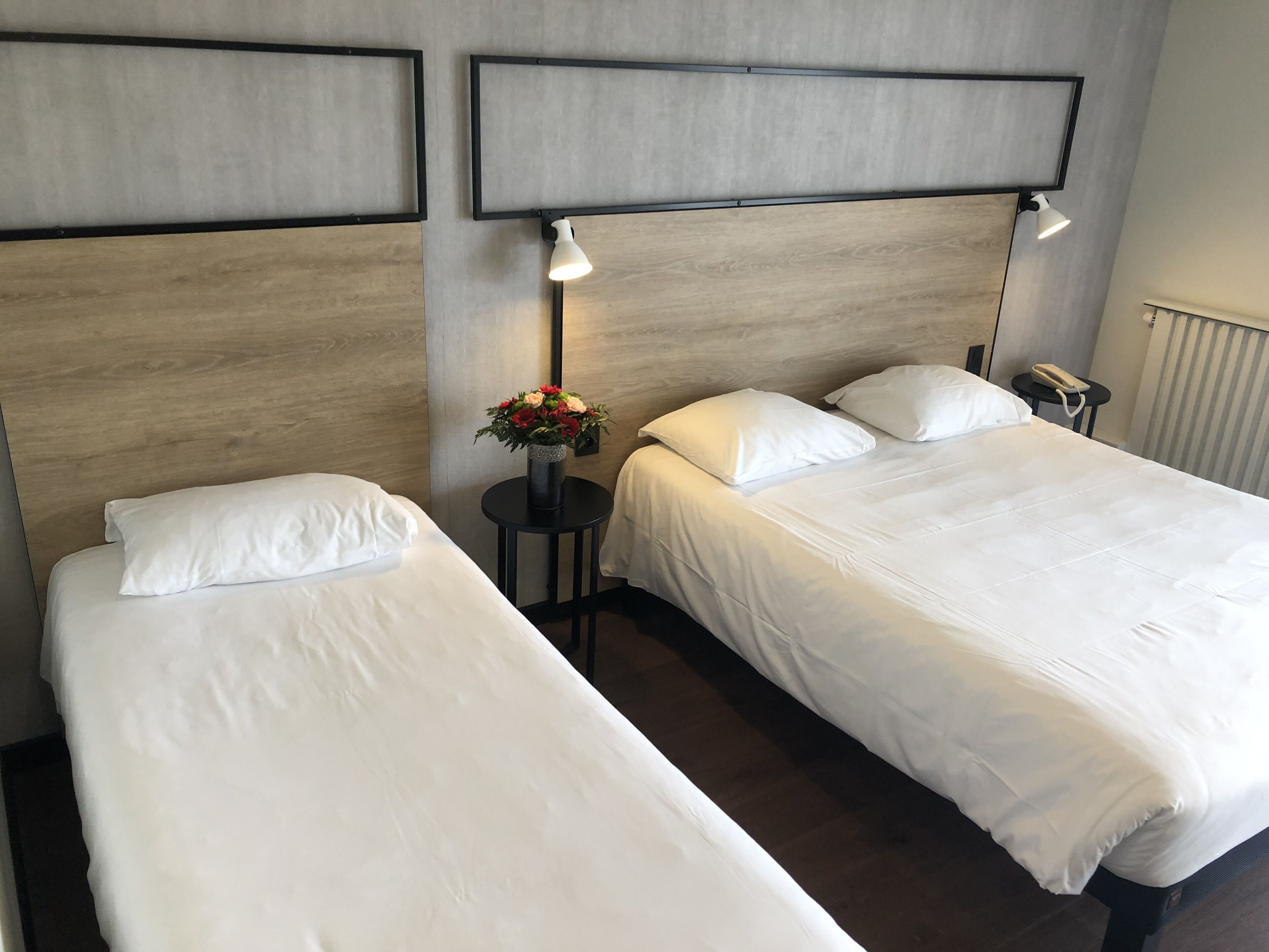 Habitación de hotel con dos camas individuales, una mesita con un florero y un teléfono en la mesita de noche.
