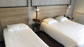 Habitación de hotel con dos camas individuales, una mesita con un florero y un teléfono en la mesita de noche.