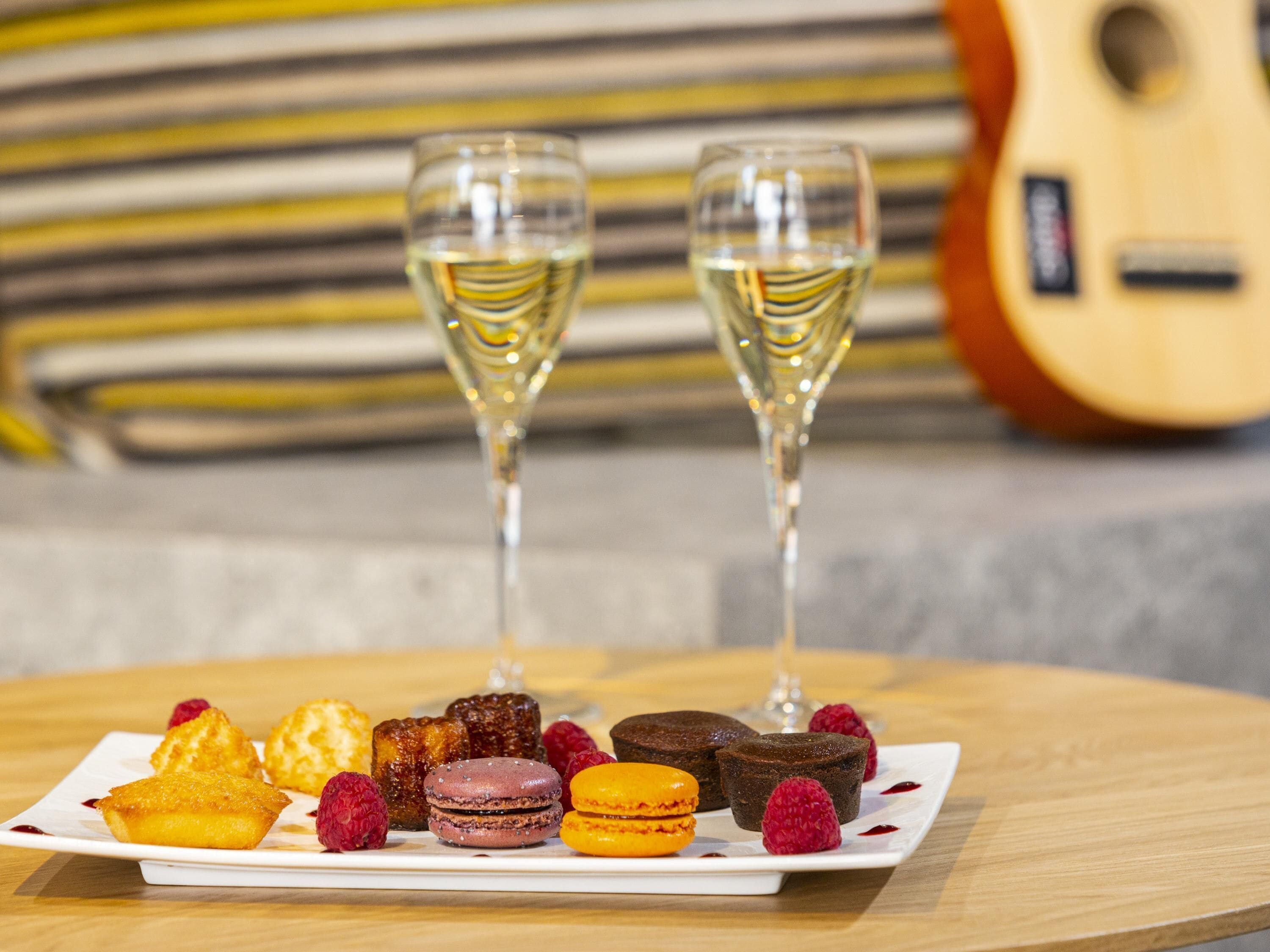 A dessert platter with various sweets and two glasses of white wine on a wooden table.