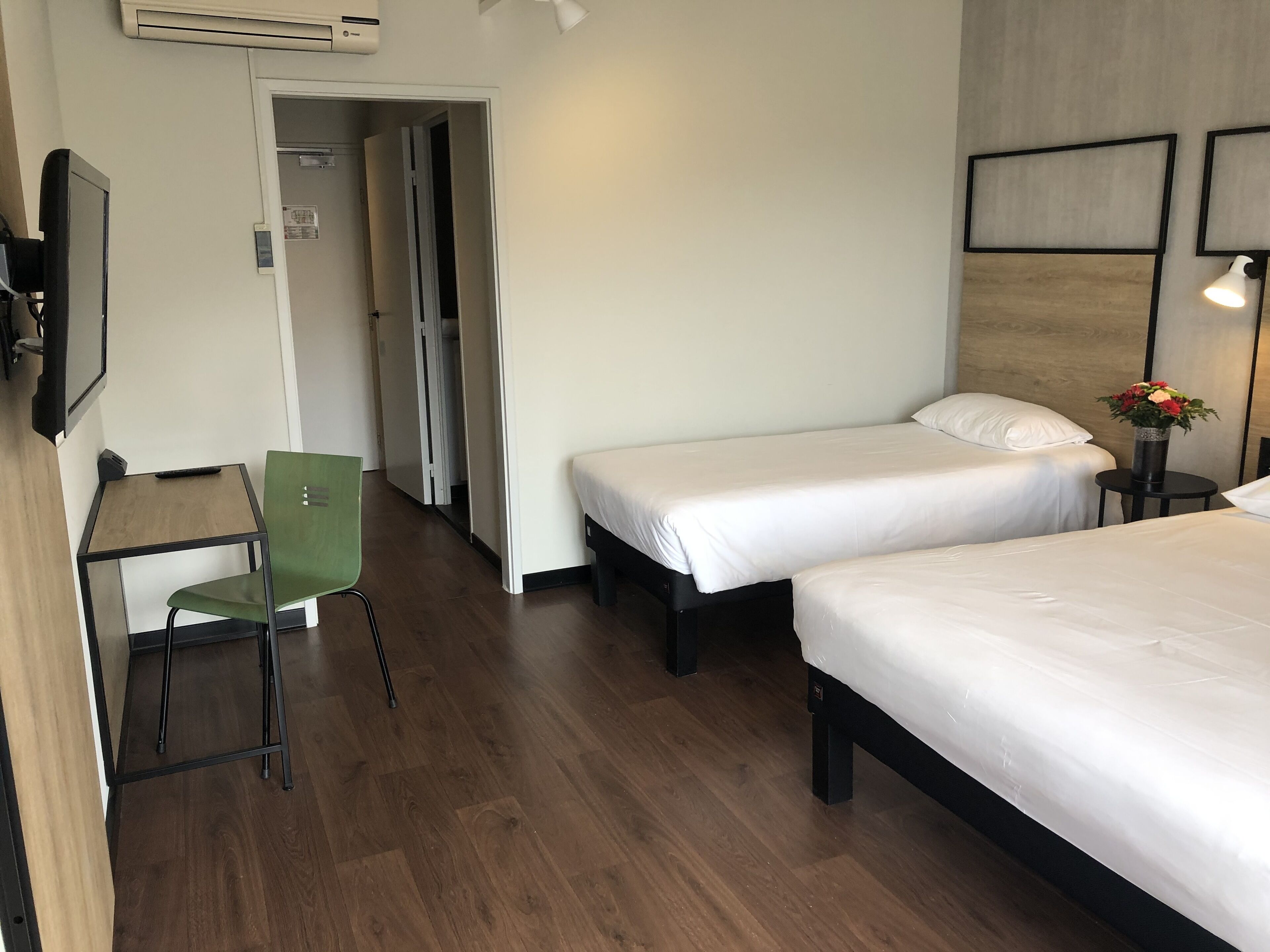 Habitación de hotel con dos camas individuales, un escritorio con una silla y una mesita con un jarrón de flores.