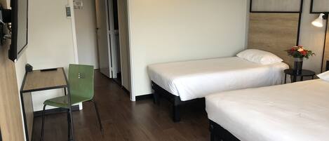 Habitación de hotel con dos camas individuales, un escritorio con una silla y una mesita con un jarrón de flores.