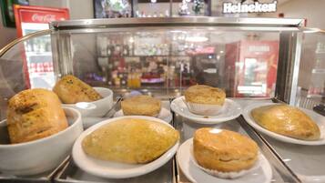 Una vitrina de panadería con diversos productos horneados, incluyendo pan y pasteles, en una tienda con la marca Coca-Cola y Heineken visible.