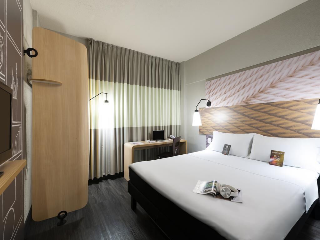 A hotel room with a bed, a desk, a chair, a TV, and a window with curtains.