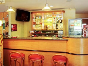Eine Barbereich mit einer Theke, Hockstühlen, einem Fernseher und Regalen mit Flaschen und Gläsern.