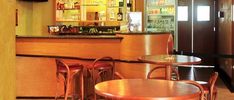 Zona de bar con taburetes, una barra y estanterías llenas de botellas y vasos.