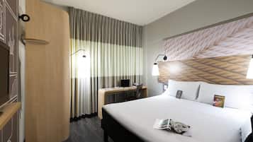 A hotel room with a bed, a desk, a chair, a nightstand, a lamp, and a wall-mounted TV.