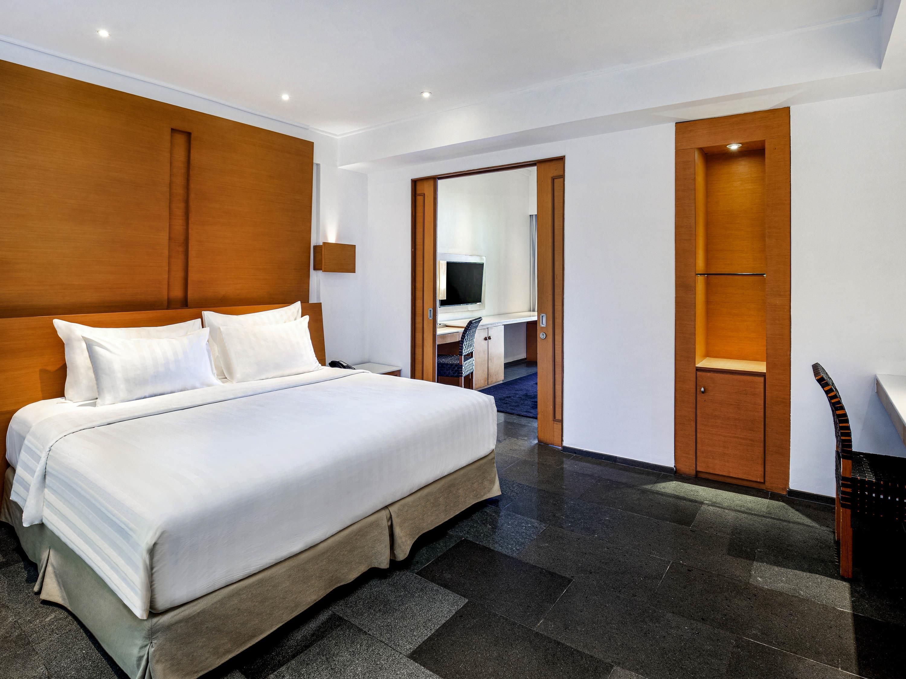 A hotel room with a large bed, a desk with a chair, a television, and a wardrobe.