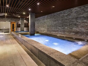 A spa area with a stone wall, a pool, and a wooden ceiling.