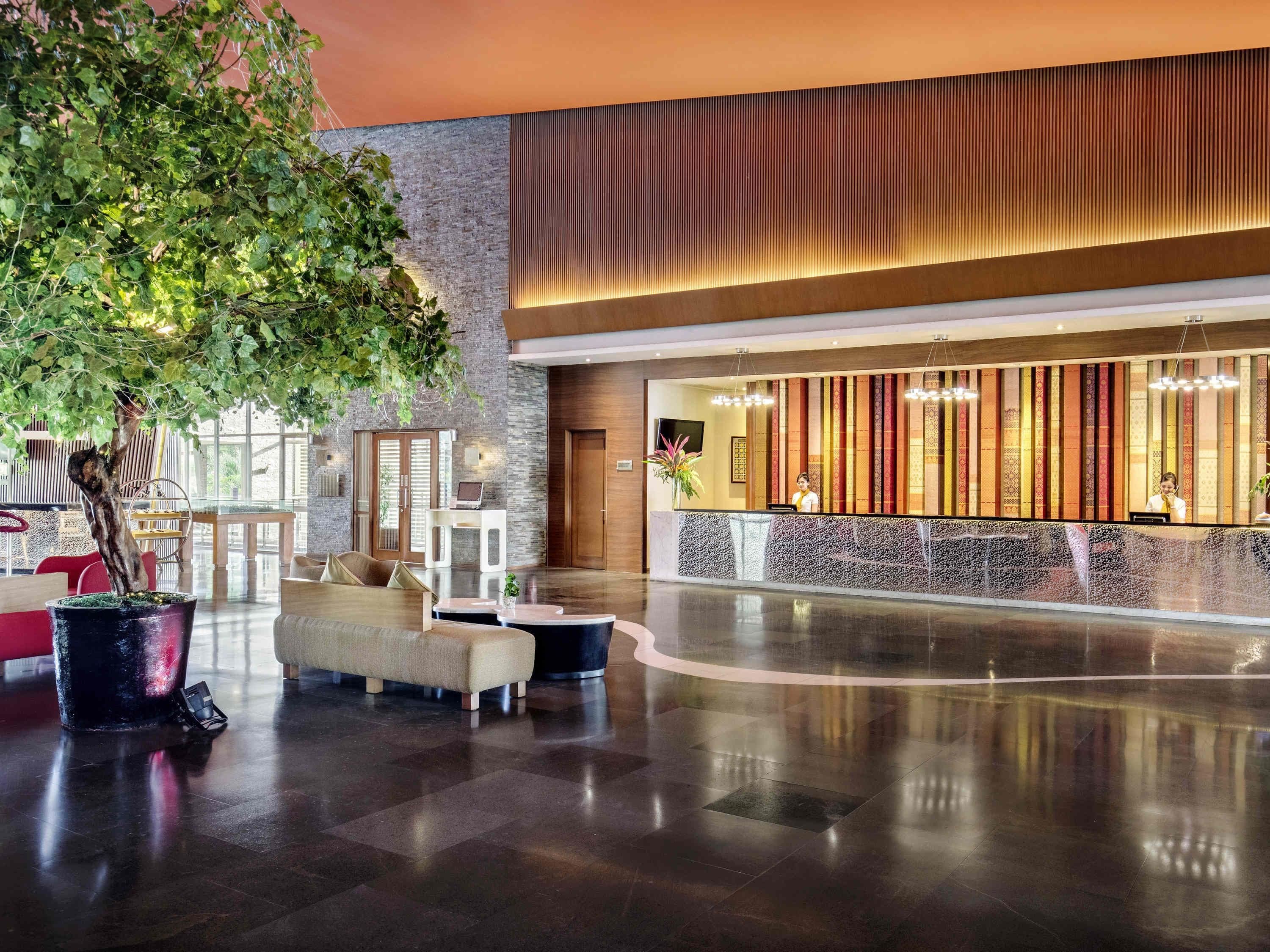 A spacious lobby with a reception desk, seating area, and a large indoor tree.