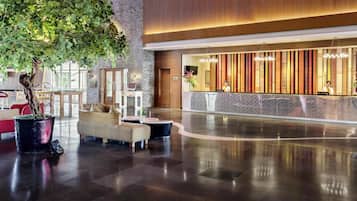 A spacious lobby with a reception desk, seating area, and a large indoor tree.