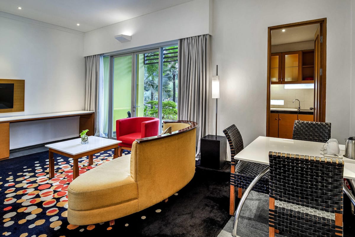 Een hotelkamer met een bank, een eettafel, een televisie en uitzicht op groen.