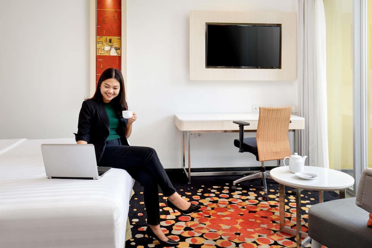Hotellihuone, jossa on sänky, työpöytä, televisio, sohvapöytä ja kuviollinen lattia.