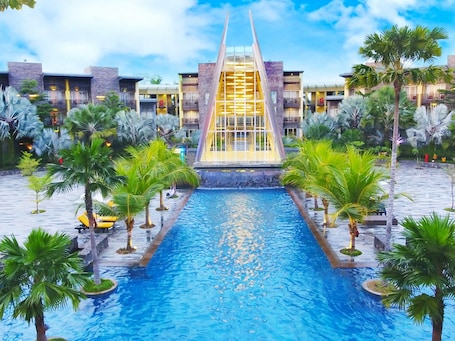 A pool area with a central water feature, surrounded by palm trees and modern buildings with balconies.. Novotel Palembang Hotel & Residence