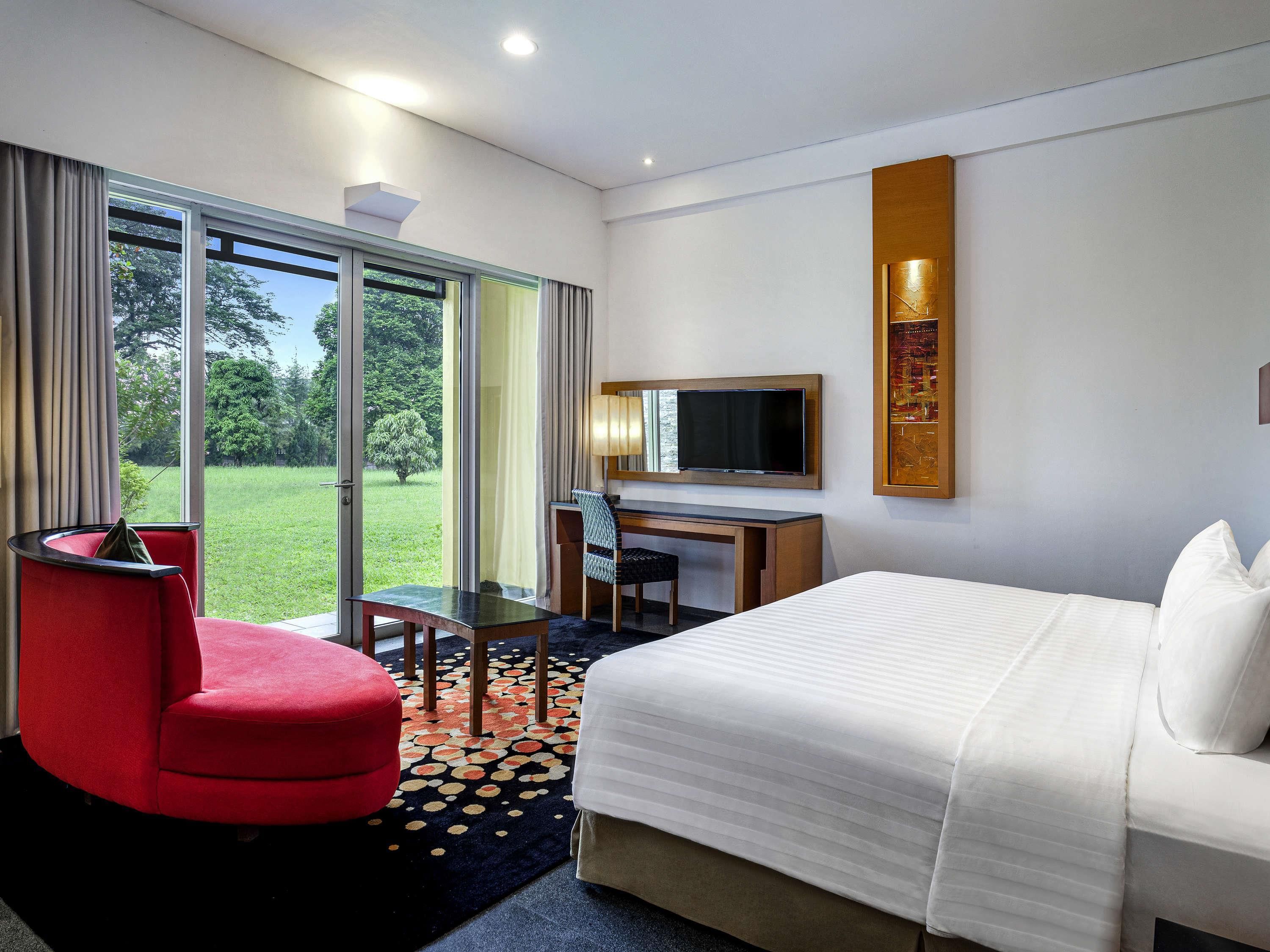 Una habitación de hotel con una cama, un escritorio, una silla y un sillón rojo.