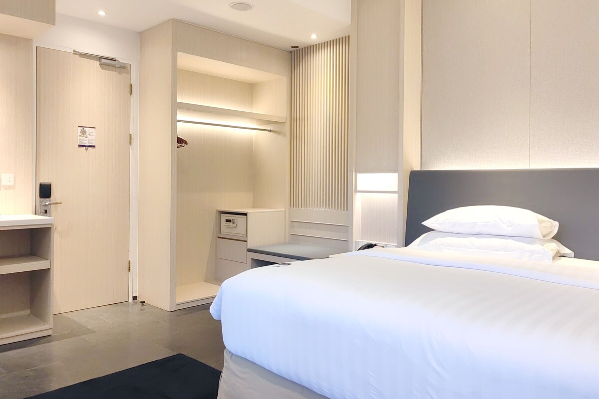 Et hotelværelse med seng, skrivebord, garderobe og badeværelse.
