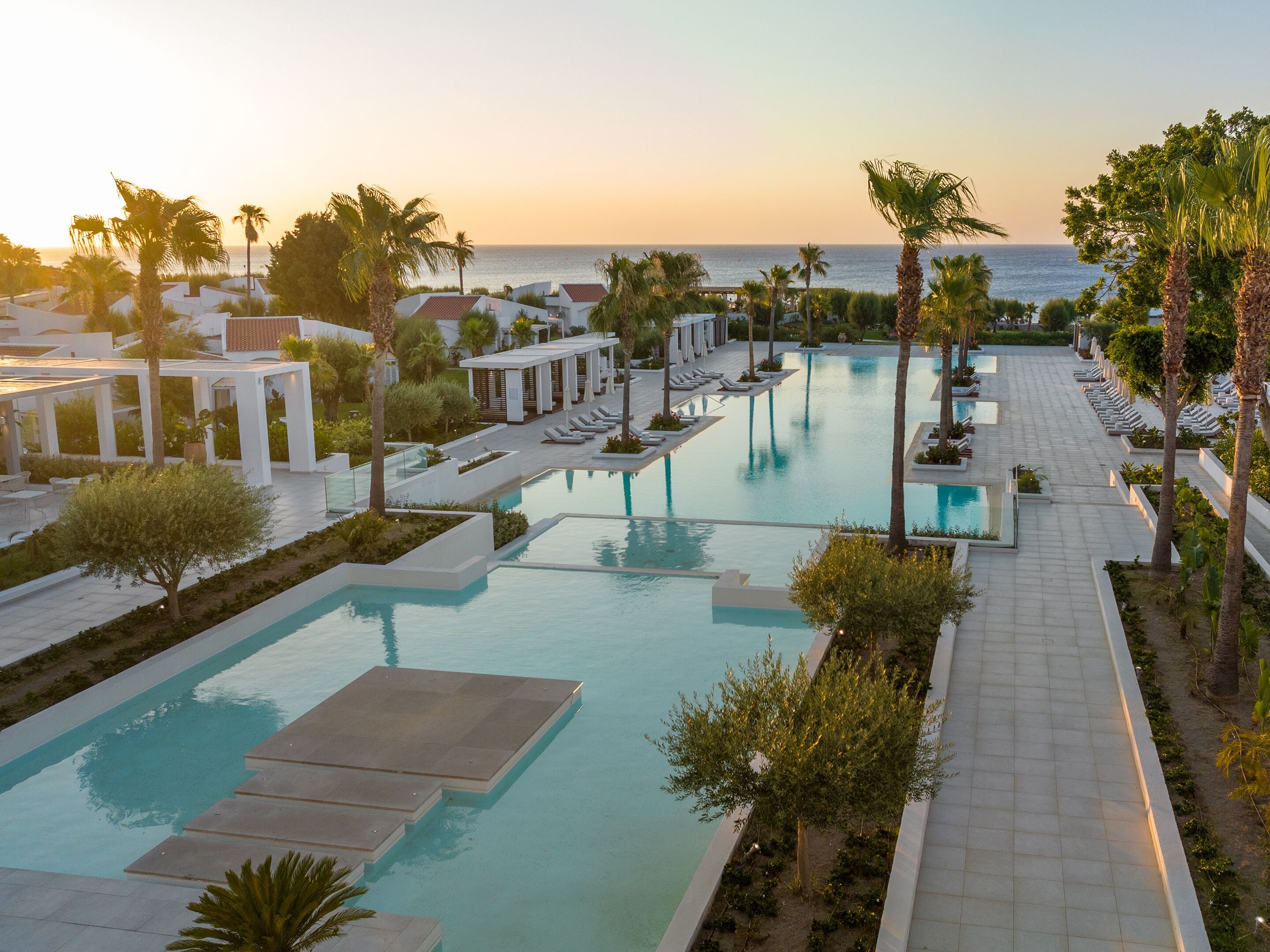 A resort pool area with multiple swimming pools, sun loungers, and palm trees.