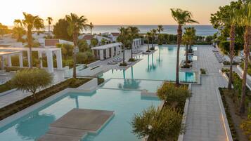 A resort pool area with multiple swimming pools, sun loungers, and palm trees.