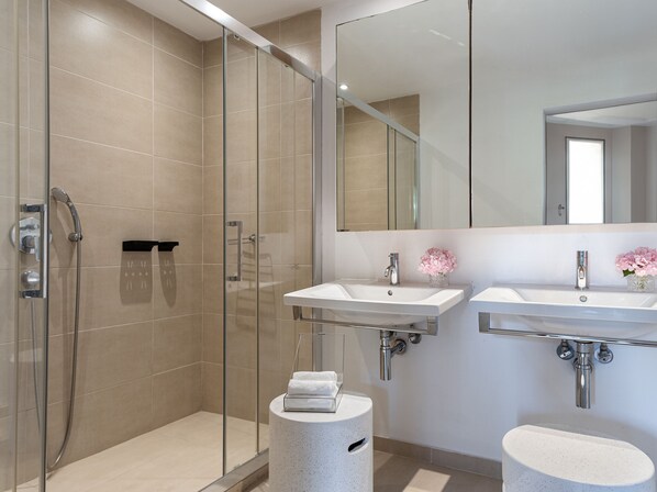 Un baño moderno con ducha envuelta en vidrio, dos lavamanos y un espejo grande.