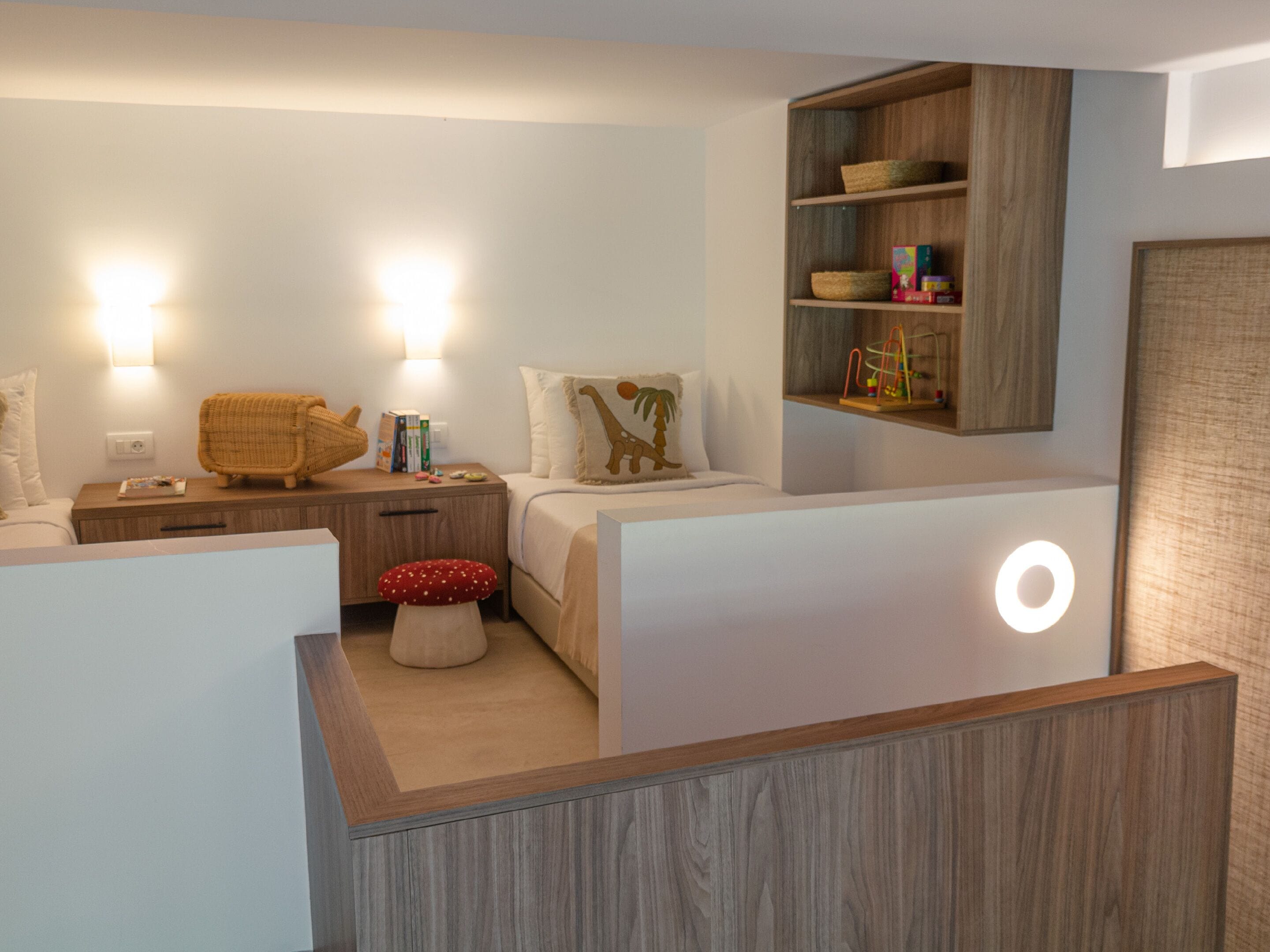 A modern bedroom with a wooden nightstand, a small stool, a bookshelf, and a wall-mounted shelf.