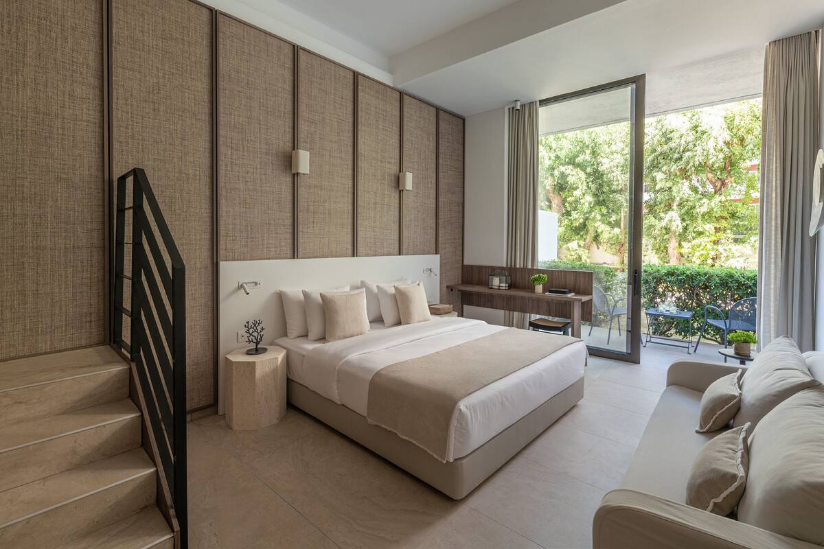 Ein modernes Schlafzimmer mit einem großen Bett, einem Schreibtisch und Blick auf einen Garten durch eine Schiebetür.